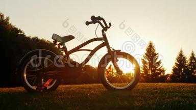 孩子们`自行车站在夕阳背景下的绿色草坪上。 概念-孩子们`梦想，快乐
